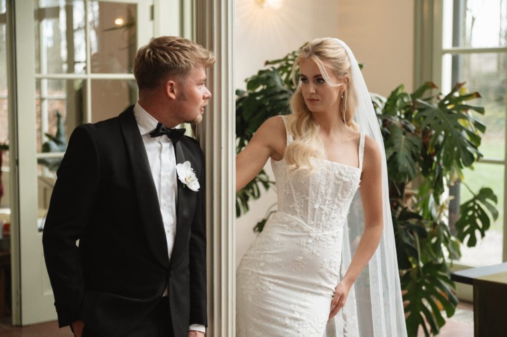 Wat is editorial bruiloftsfotografie en waarom is het zo populair? Bruidspaar kijkt verliefd naar elkaar tijdens hun bruiloft, bruid draagt een witte jurk en bruidegom een classy zwart pak.