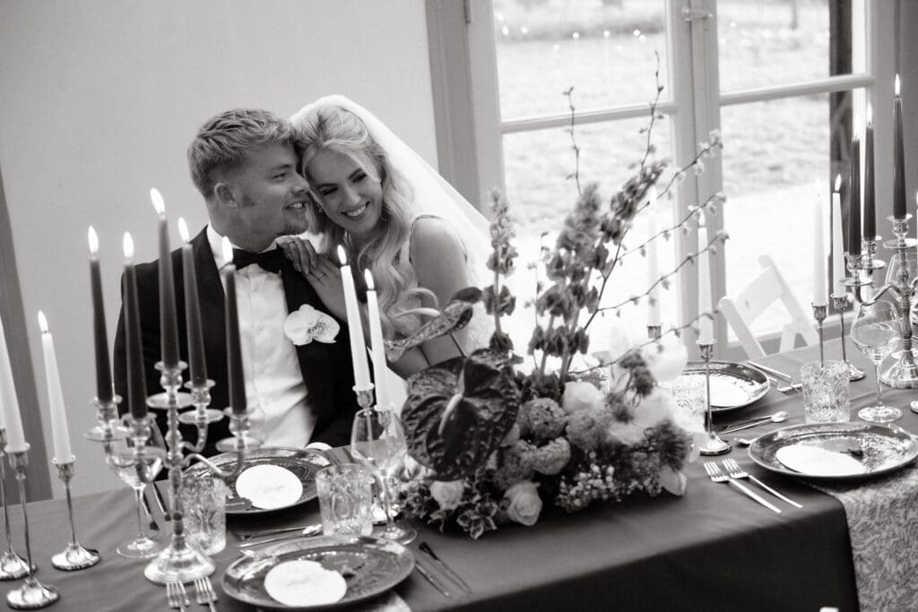 Tips voor een ontspannen bruiloft. Verliefd bruidspaar aan een mooie gedekte tafel met kaasren en bloemen tijdens hun bruiloft.