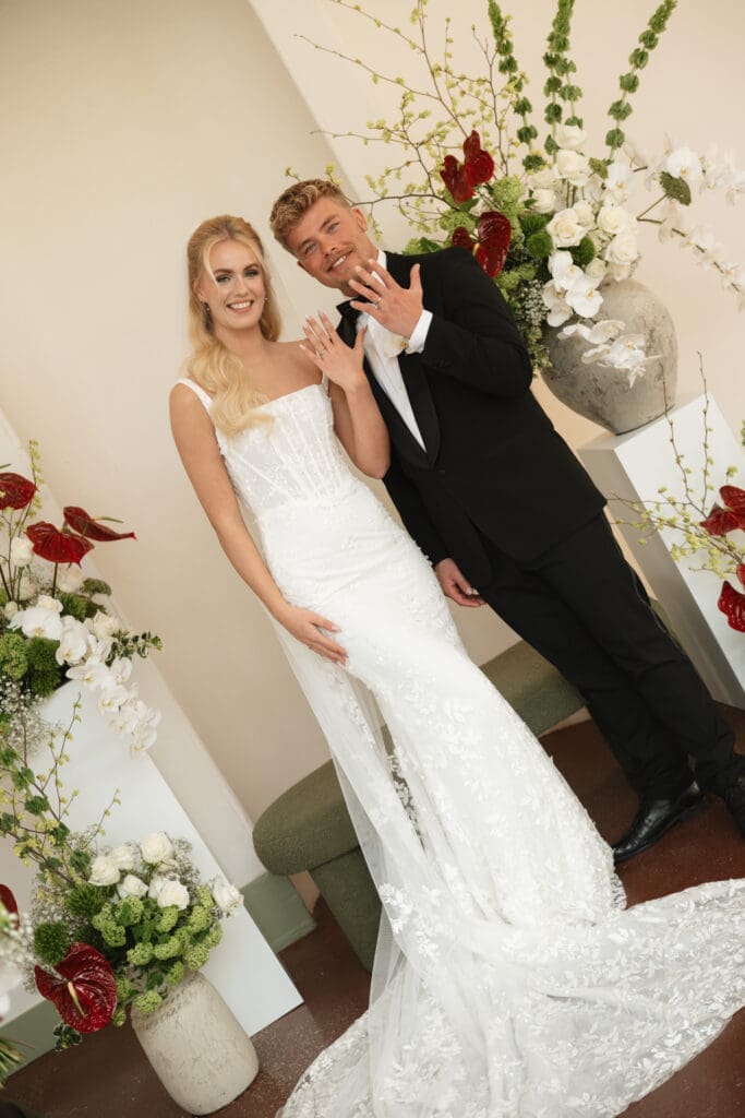 Trouwen bij de Oranjerie op Landgoed Vollenhove. Bruidspaar laat hun trouwringen zien, omringd door bloemen. De bruid draagt een jurk van MWL Bride