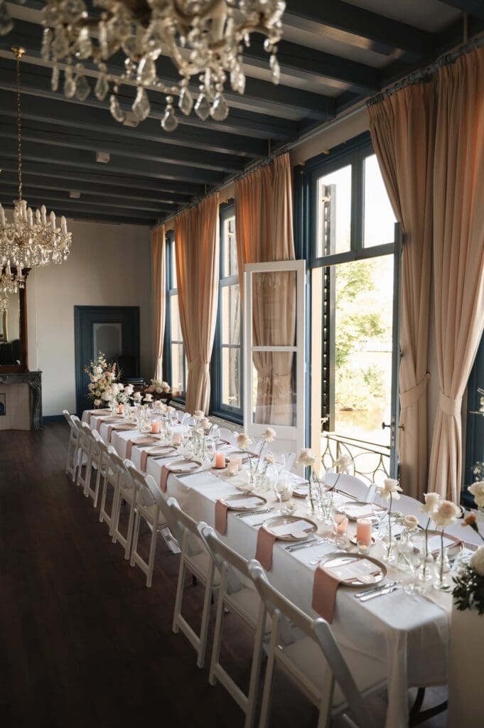Trouwen bij Landgoed huis Brakel, stijlvol gedekte tafel met bloemen en roze servetten, bij openslaande deuren